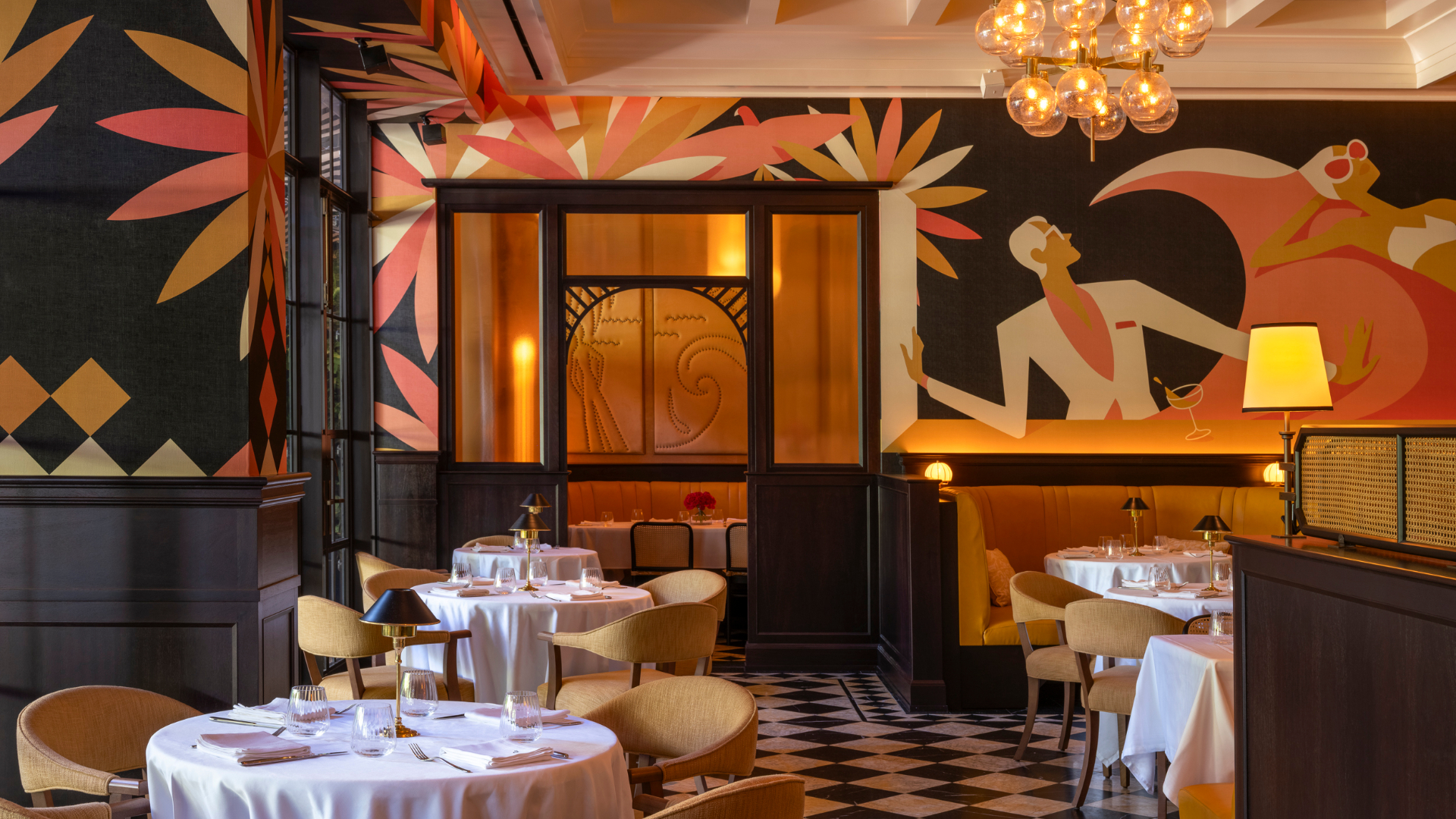 An elegant restaurant dining room with white-clothed tables, warm lighting, and bold Art Deco-inspired murals in orange, pink, and gold tones.